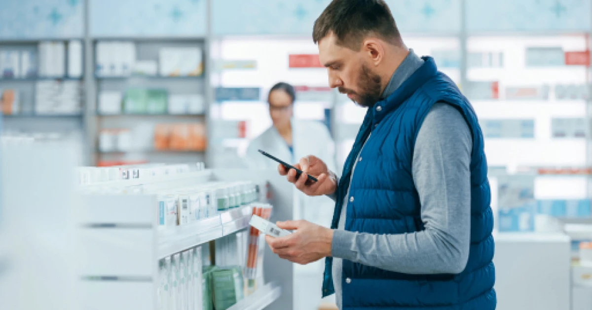 Man using smartphone to check medical advice in a pharmacy.