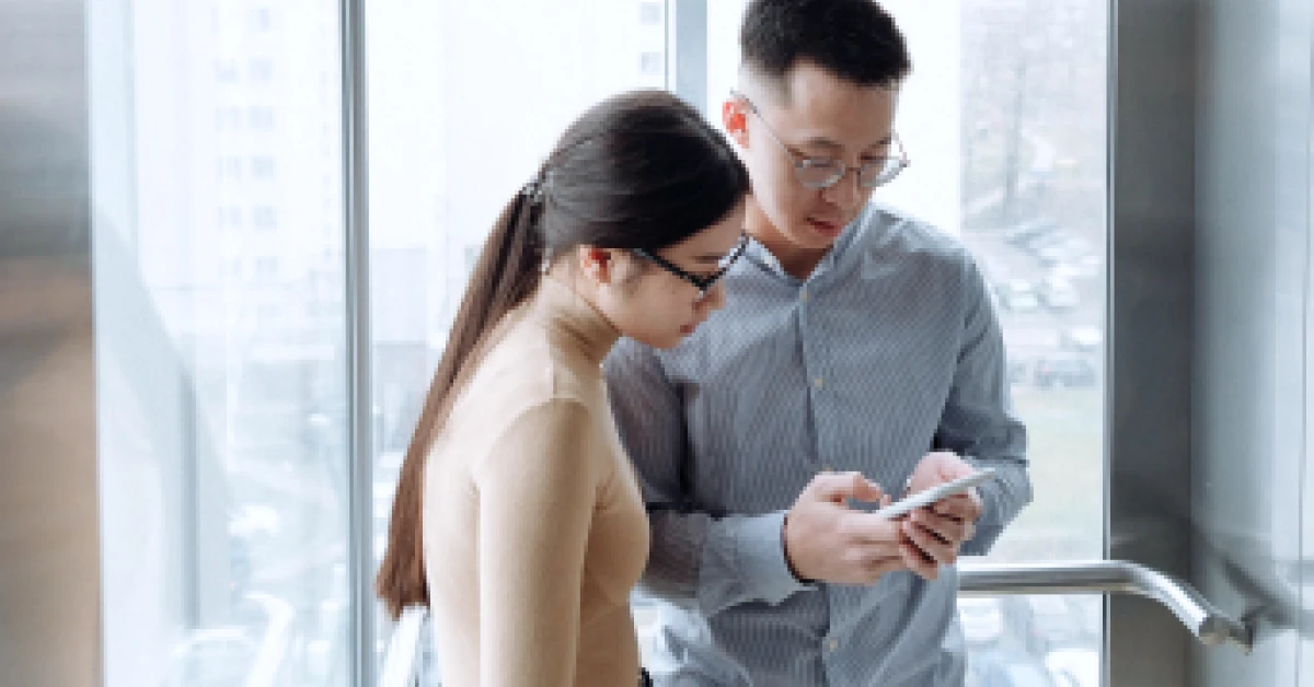 A man and woman looking at a smartphone inside the elevator.