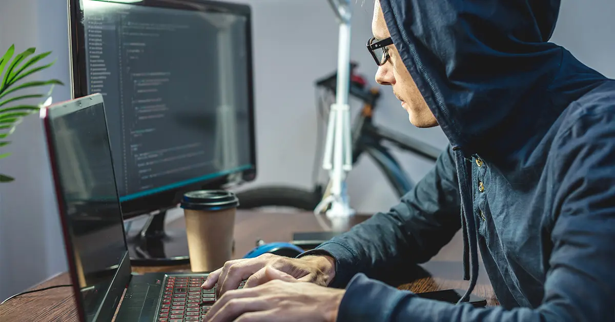 Person with hood typing on laptop.