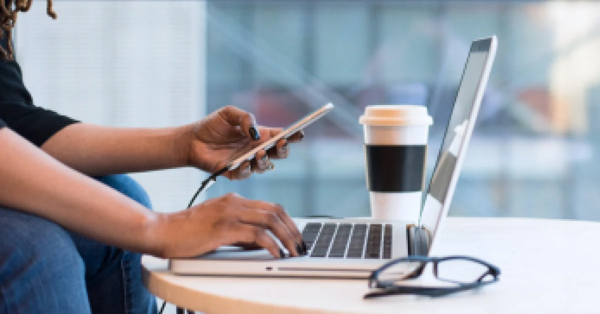 Woman using mobile phone and laptop in an open plan office.