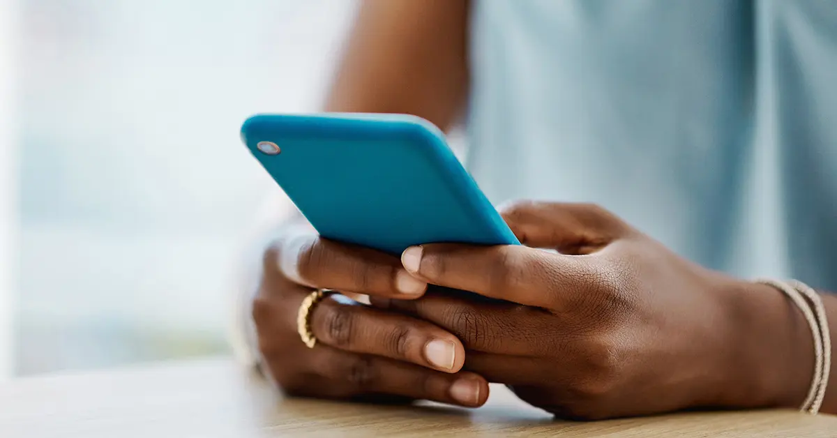 Person holding a phone, resting their hands on a table.