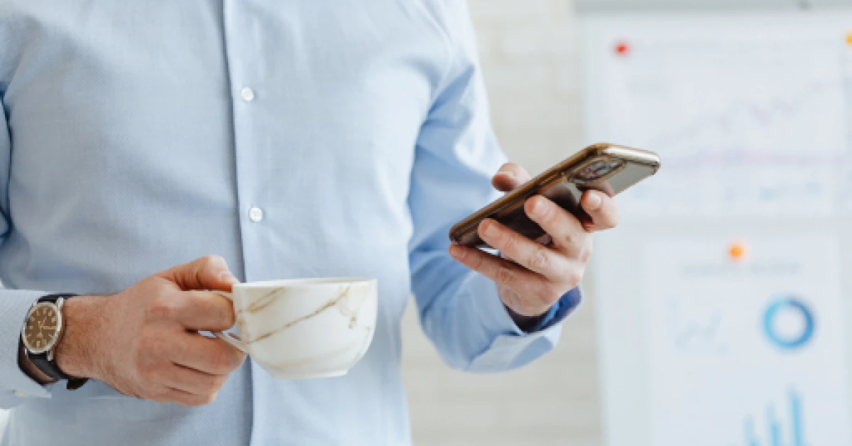Man holding a cup and using a smartphone.