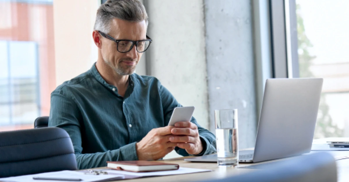 Smiling businessman holding smartphone sitting in office.