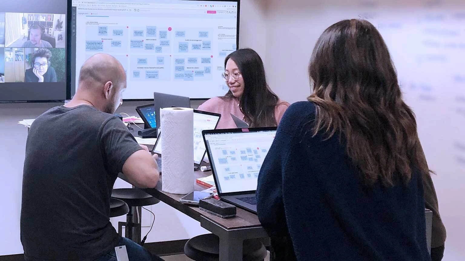 Three UserTesting workers are using mural on a big monitor to work together with a team on video call.