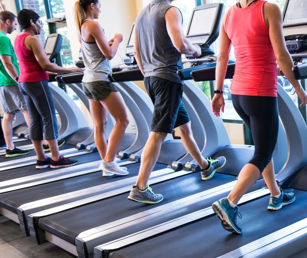 five people walking on treadmills at the gym