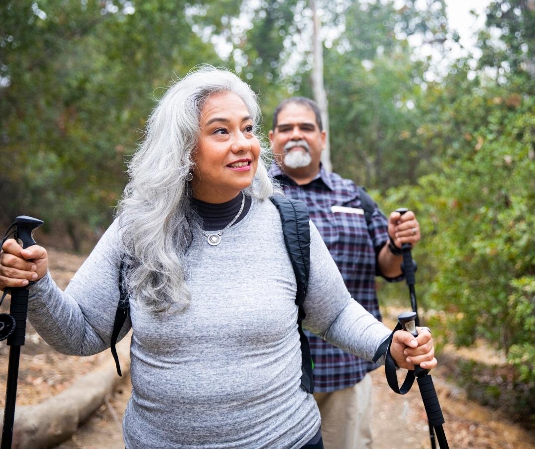 middle aged couple hiking in the woods using walking poles for balance