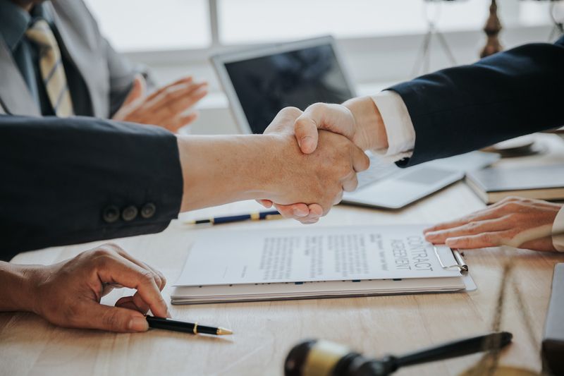 A pair of business men across a table shaking hands