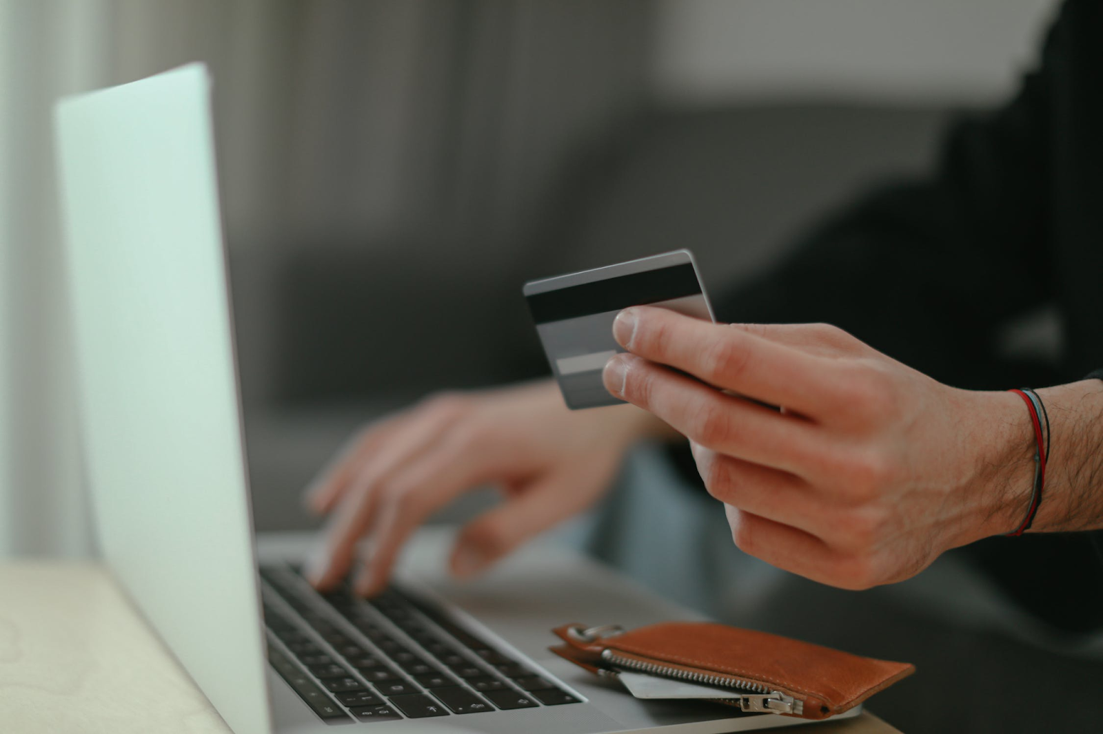 A photo of a man typing on a laptop keyboard with one hand and holding a credit card in the other