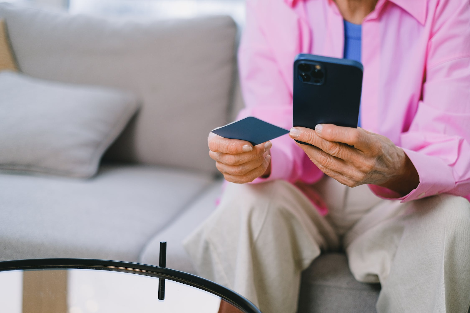 A photo of a seated person using a smartphone while holding a credit card