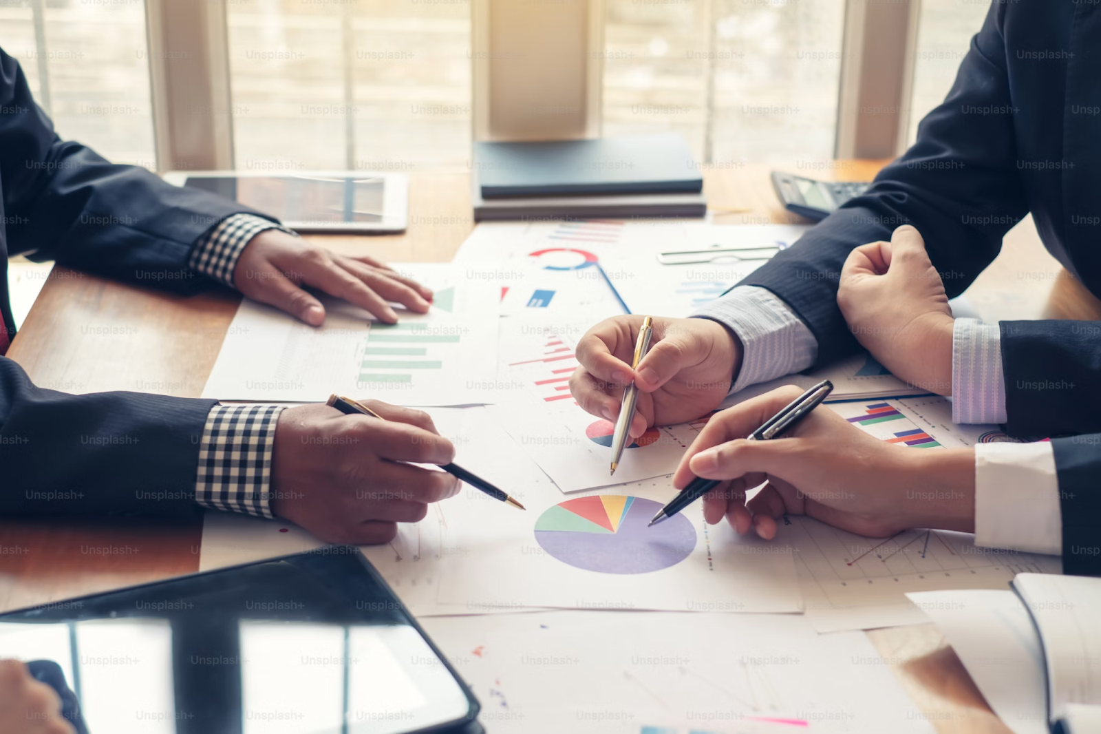 A photo of business people pointing at financial data papers placed on a table