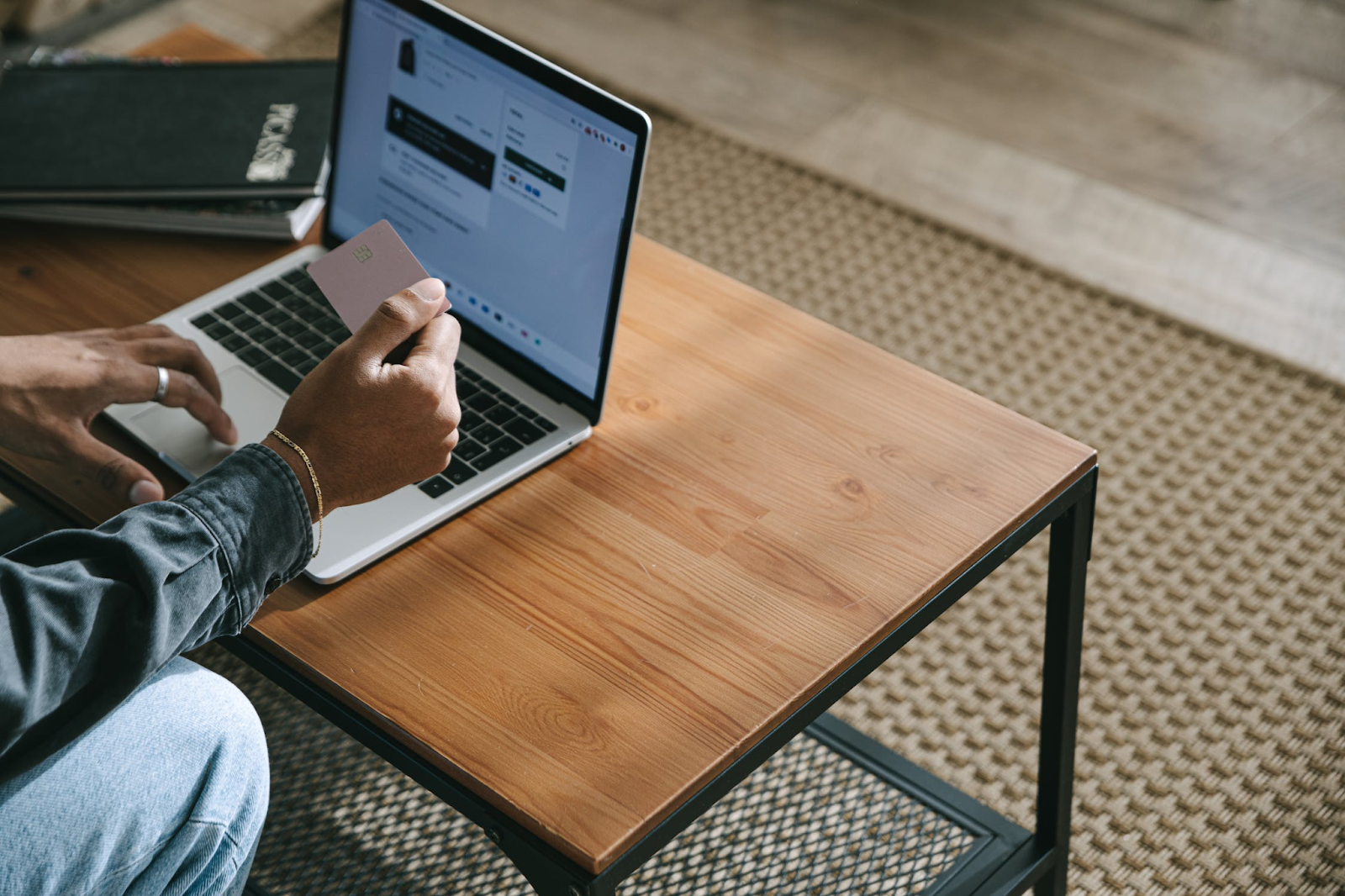 A photo of a person holding a payment card while using a laptop placed on a wooden coffee table