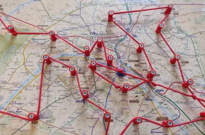 A printed map of Paris with red pins stuck in a number of locations. A red string winds around the pins, creating a route.