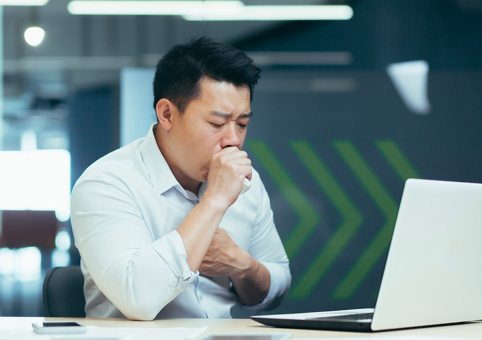 Picture of a man with asthma sitting at his desk and coughing.