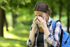 Picture of a woman sneezing with trees in the background.