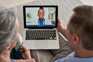 Over shoulder view of old grandparents couple patients video calling virtual doctor using laptop at home