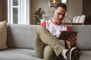 Picture of a man sitting on a couch and using a tablet.
