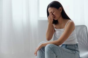 Picture of a woman with a sinus infection sitting on a chair and holding her upper nose in pain.