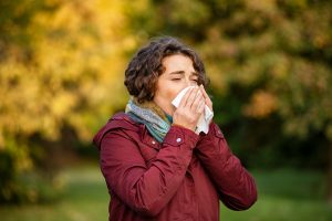 Picture of a sick woman coughing into a tissue while standing outside.