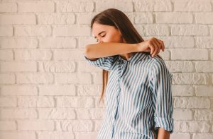 Picture of a sick woman coughing into her elbow.