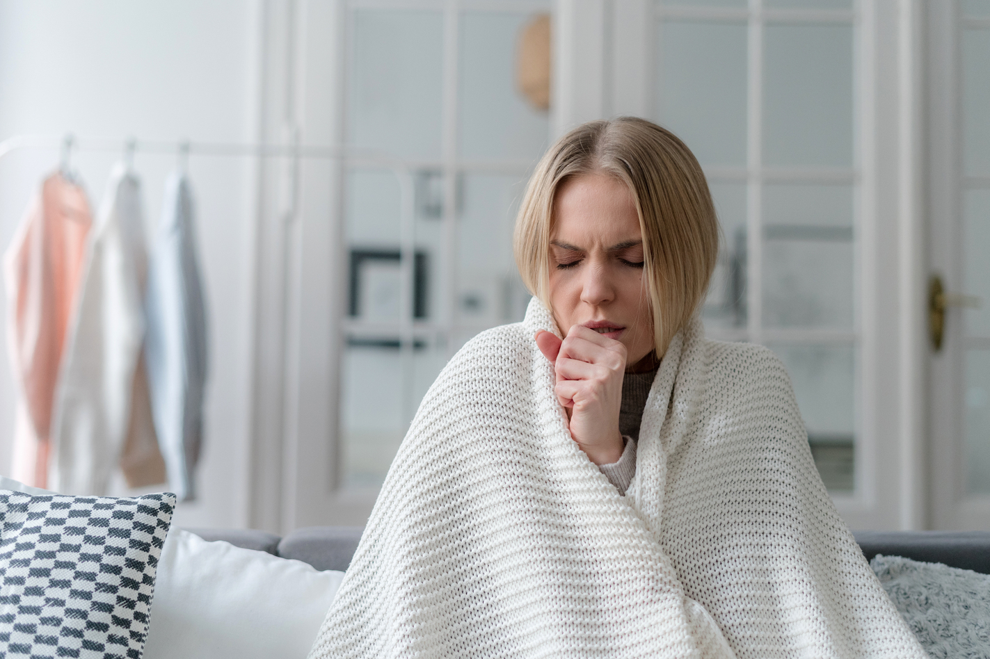 Picture of a woman with bronchitis sitting under a blanket and coughing.