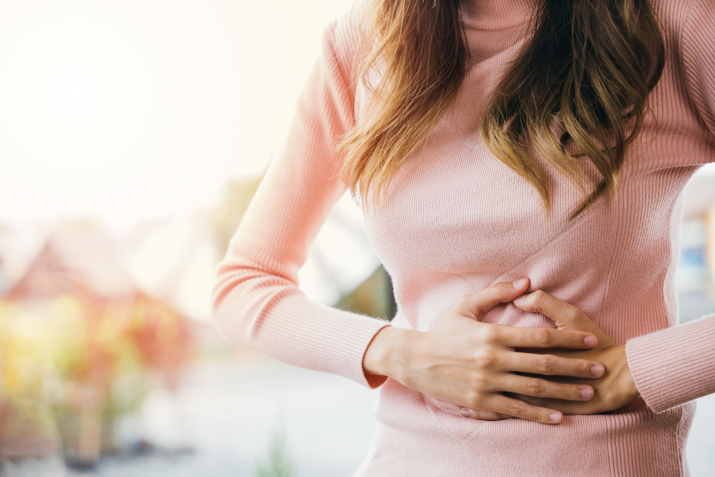 Woman holds her stomach as it pains her.