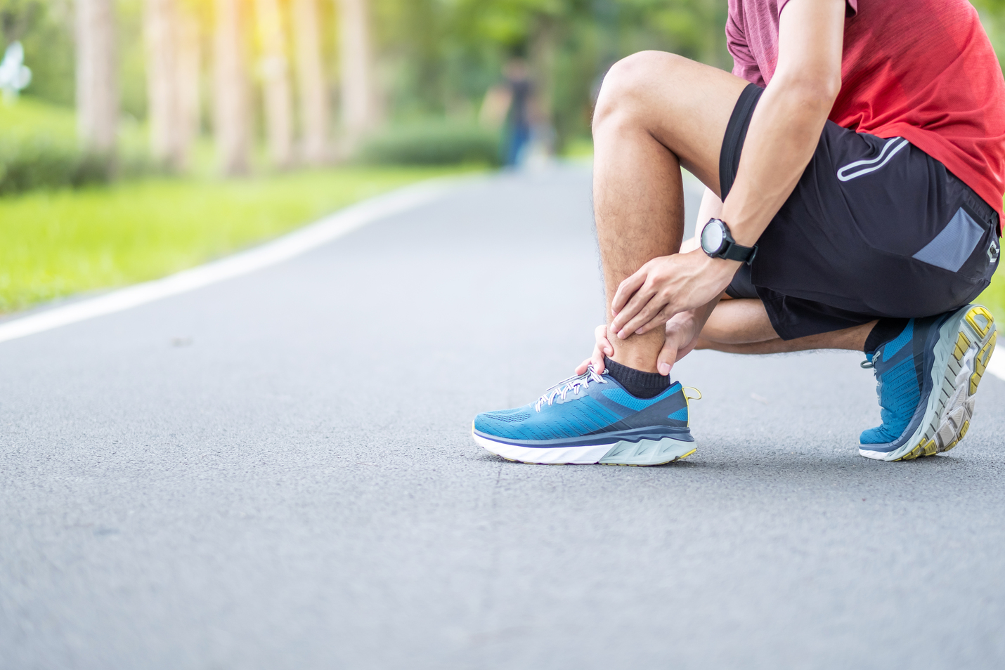 Picture of a man with a leg injury kneeling down on a running track and holding his calf in pain.