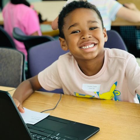Kid smiling with a laptop on his desk