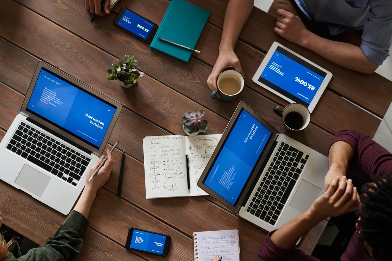 people around a table showing their laptops and tablets