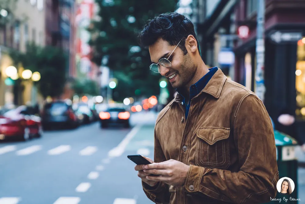 Man wearing a suede jacket on a city street in the evening, looking at his phone