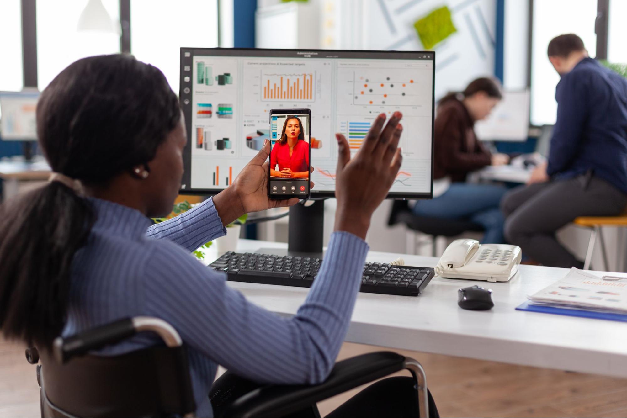 African-American woman wheelchair user, greeting someone on her phone in an office. 