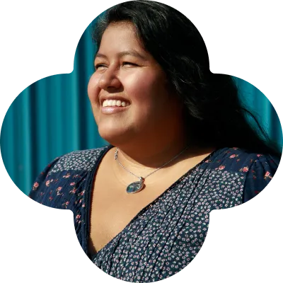 Photo of Frances in front of a blue wall looking into the distance masked in a flower shape