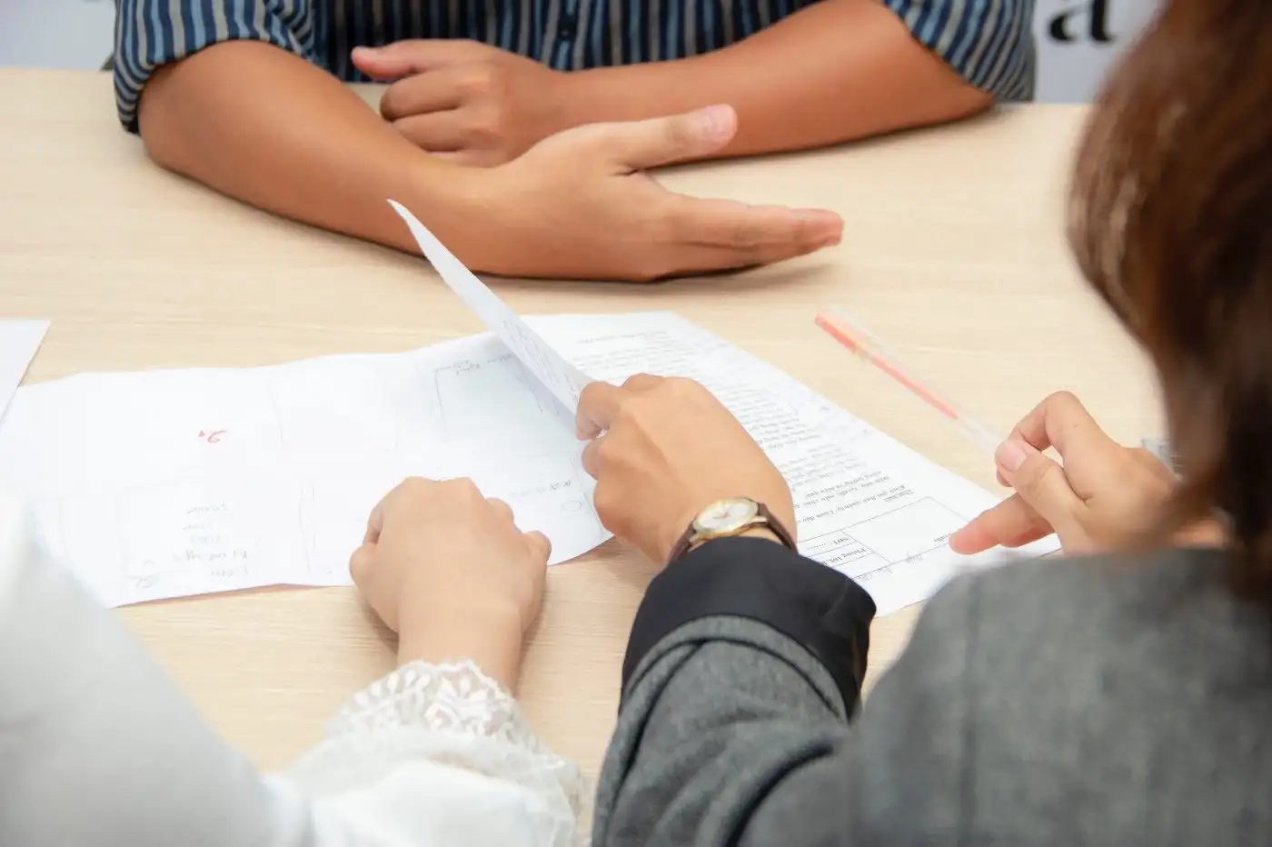 Three people sitting together with their arms on a table, looking through papers and holding a pen.