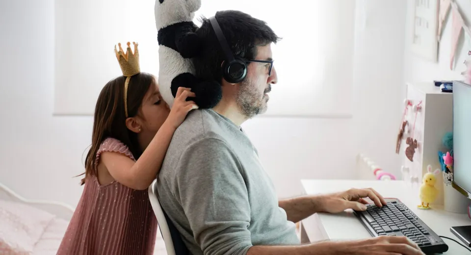 A man working on a computer, while a while distracts him from behind