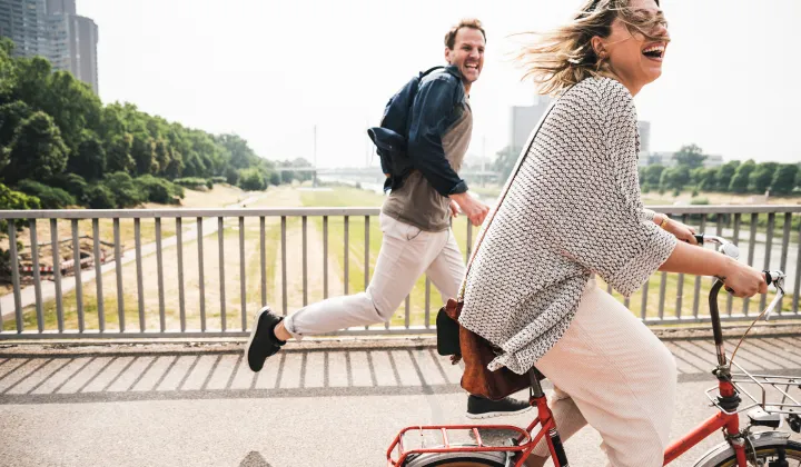 Ein Mann läuft neben einer Frau, die mit dem Fahrrad über eine Brücke fährt.