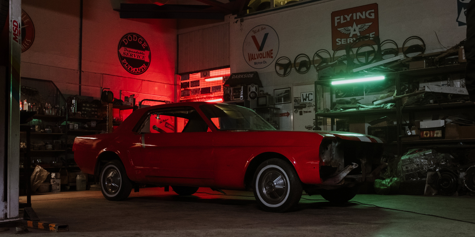 A red Mustang parked in a garage illuminated by red lights.