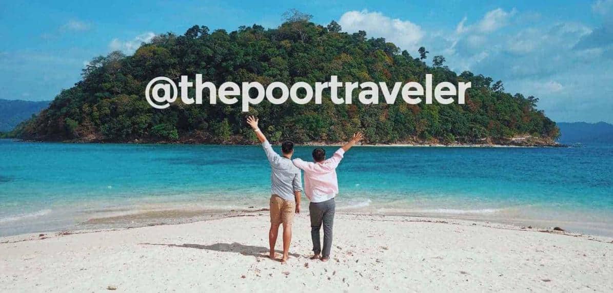 Two men raising their hands on the beach in front of an island