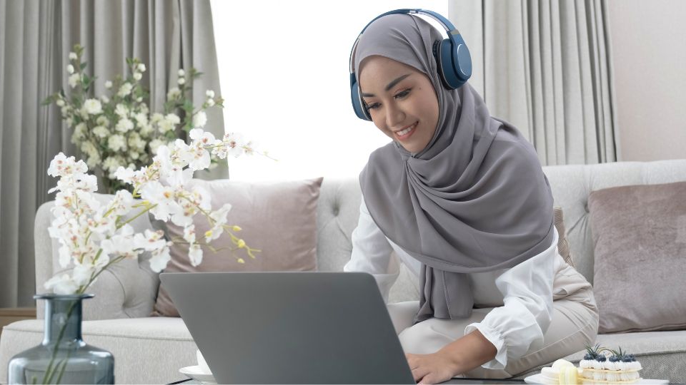 A woman editing on a laptop with headphones on and a beige living room.