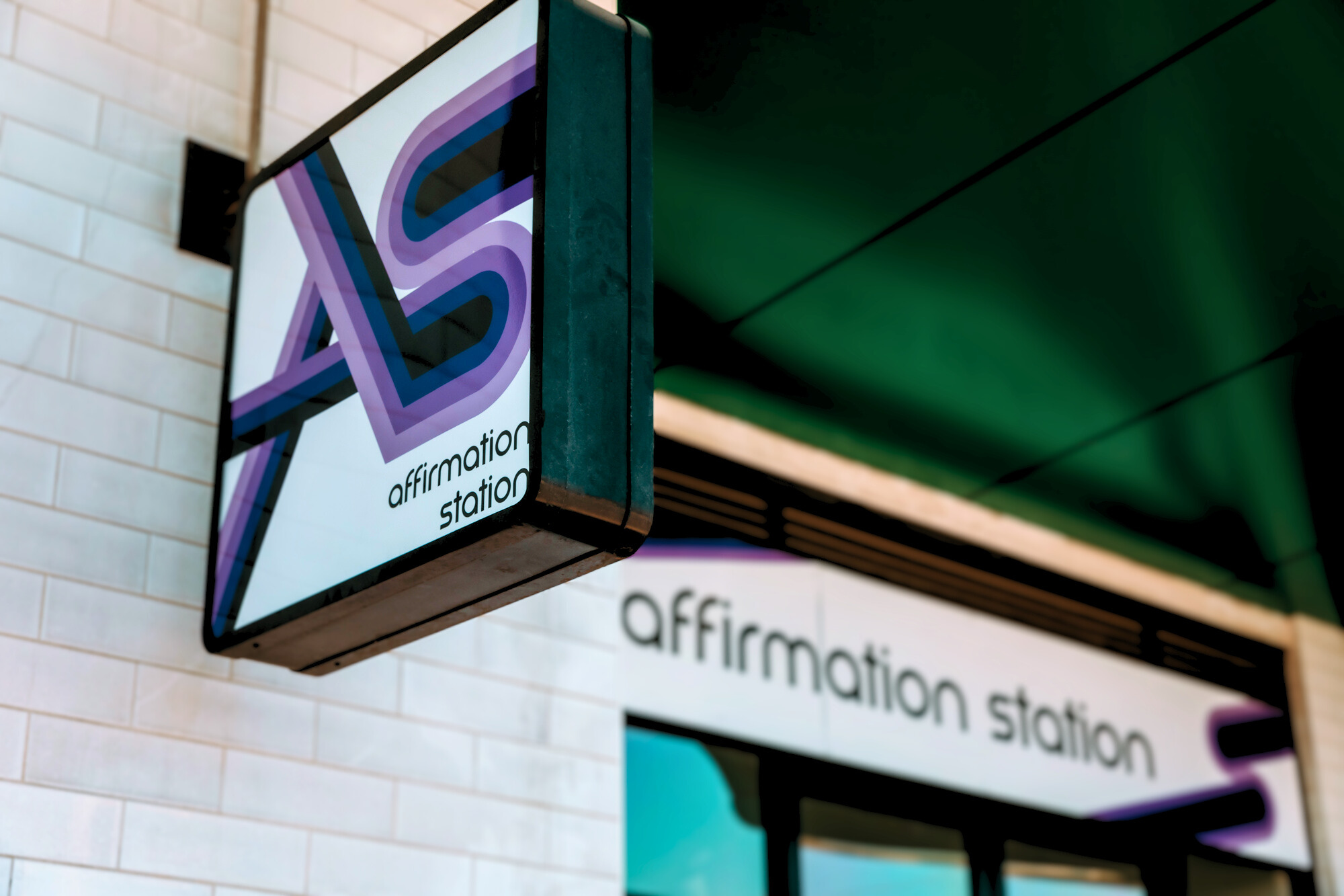 two people sitting across each other on a couch. One has bright pink and yellow hair, and is wearing a sweater. Teh other is wearing glasses, holding a clipboard and pen.