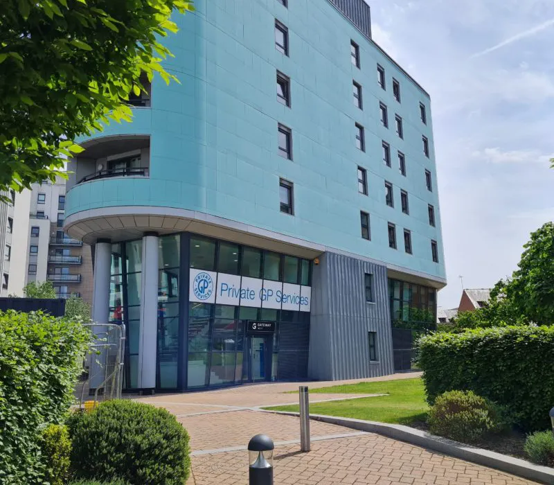 A picture of a blue clad building with glass window walls on the ground floor with a Private GP Services sign above the door.