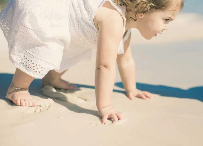 Baby in a white dress crawling on the shore down by the waves