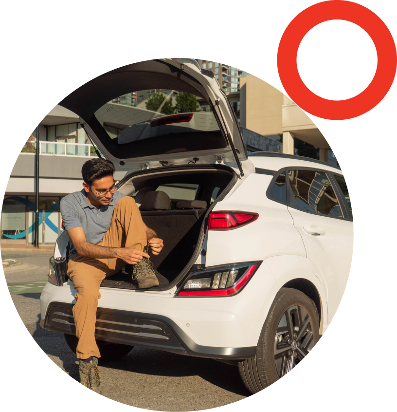 A person sitting in the back hatch of a Modo car tying up their boot.