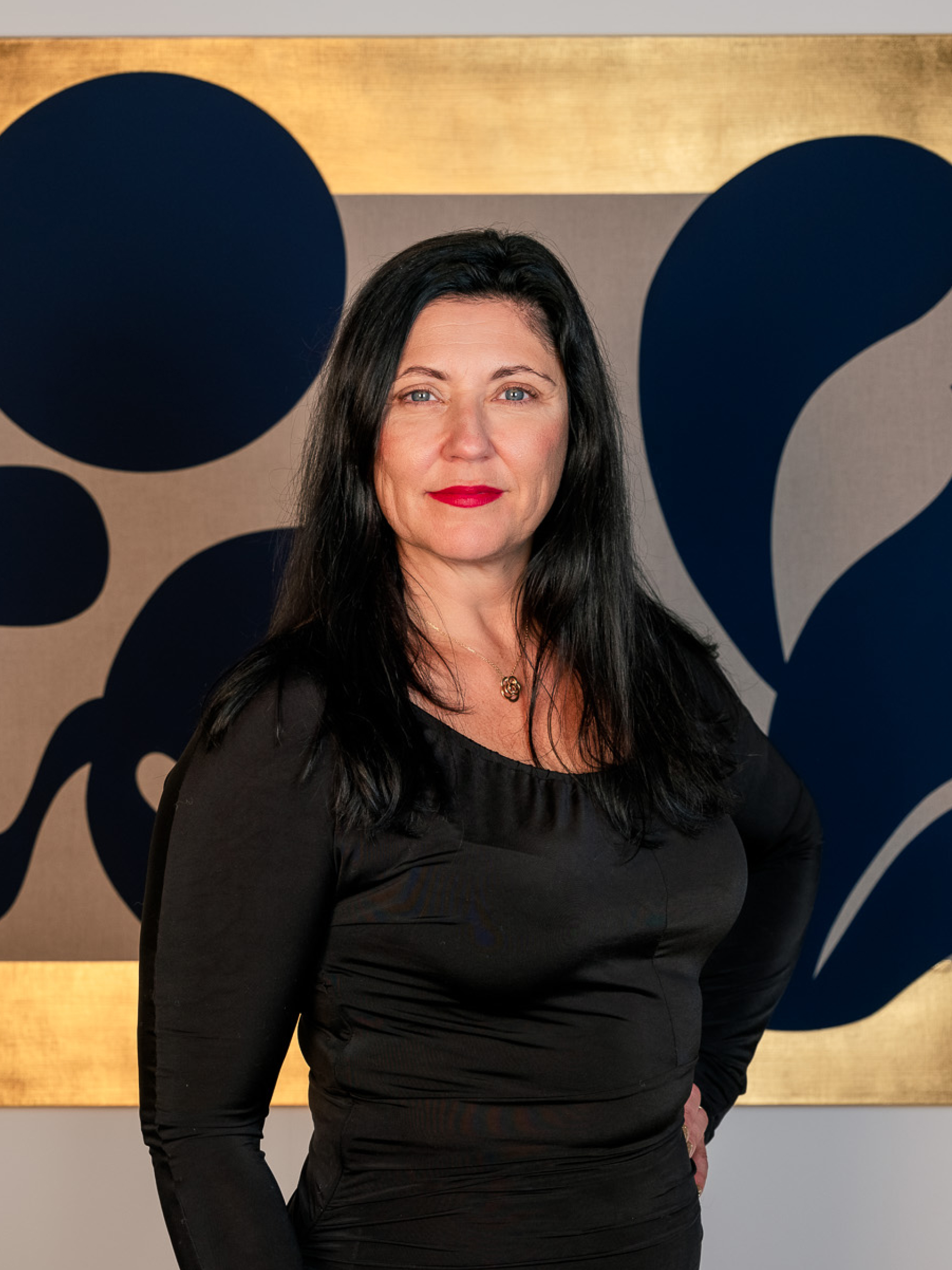 Headshot of Kristin Hjellegjerde wearing black, standing in front of a large gold painting