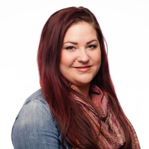 A smiling red-haired woman wearing a denim shirt and a scarf.