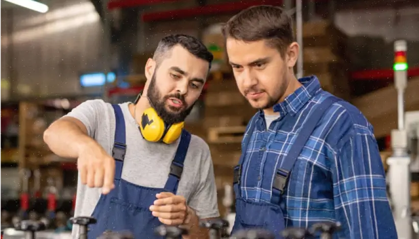 An experienced manager is cross-training an employee on an unfamiliar machine.