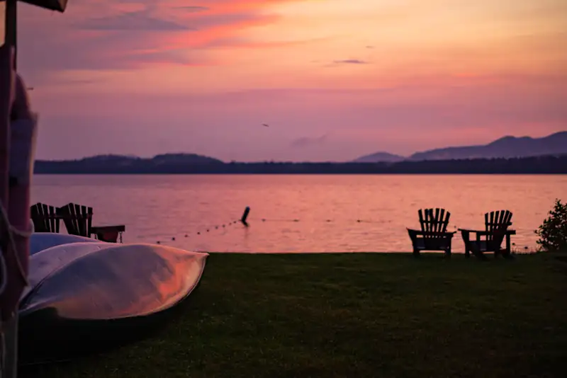 The Lake Clear Lodge & Resort lakefront with canoes during a pink, hazy sunset.