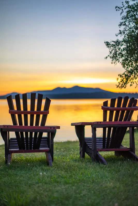 Two Adirondack Chairs at the Lake Clear Lodge Lakefront while the sun sets over Saint Regis Mountain.