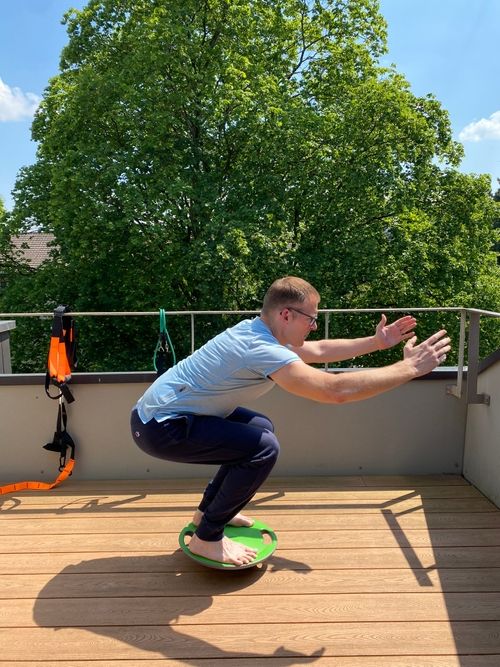 Training man in the end position doing a squat on a balance board.