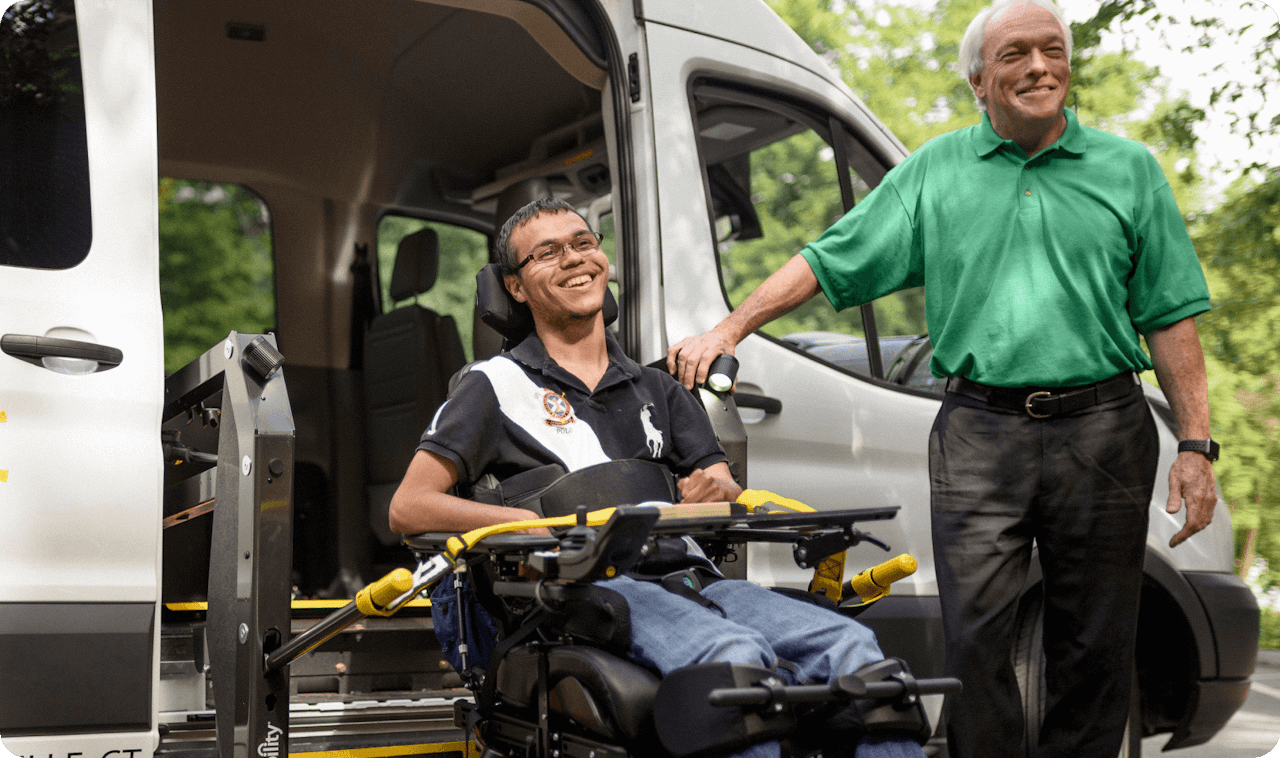 A man in a wheelchair being aided by another man. Wheelchair transportation services.