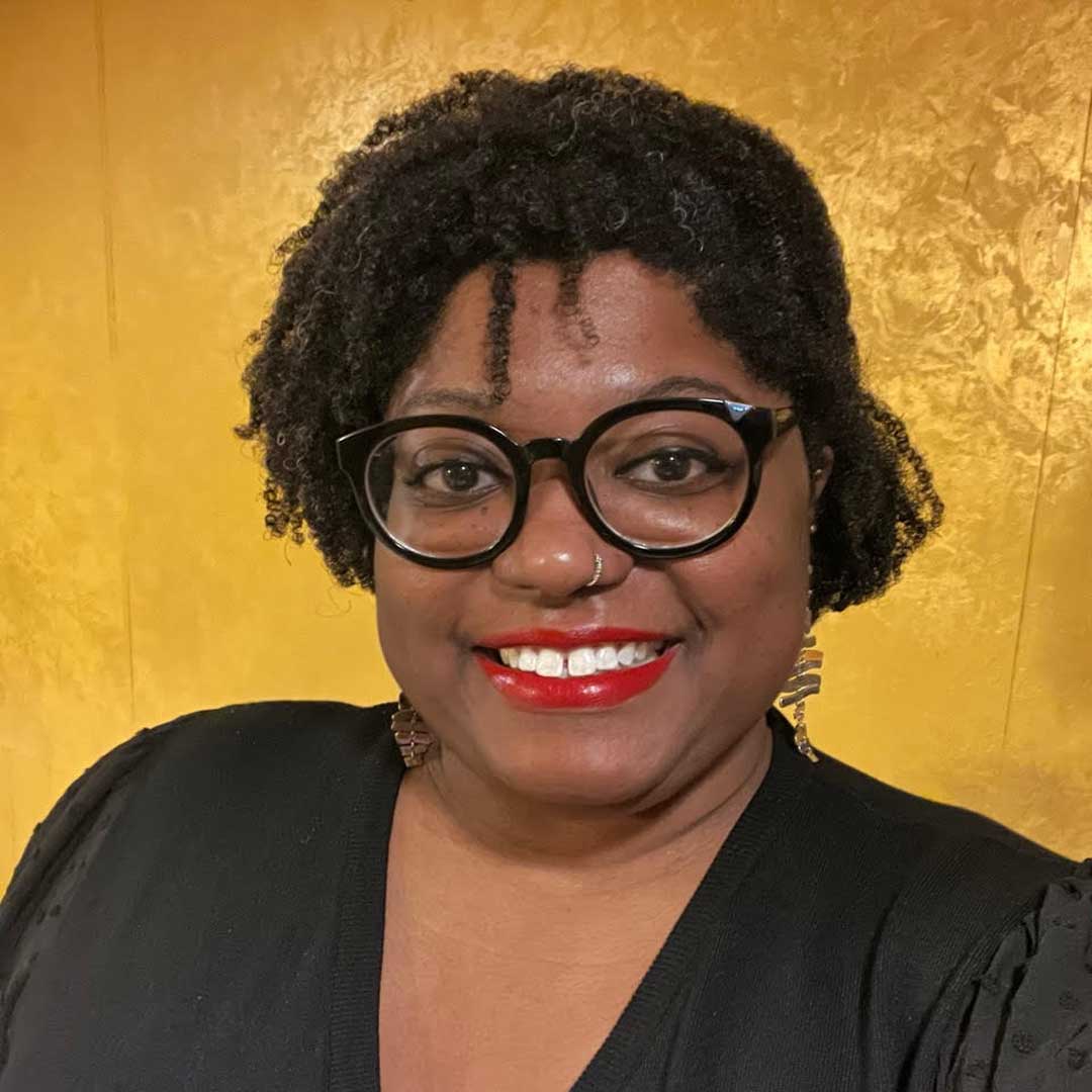 Headshot of Adjoa Sankofia Tetteh. She is smiling, wearing a black blazer, dangly earrings, and glasses.