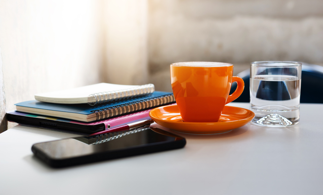 A Mug of Coffee Along with a Glass of Water, Books, Pen, Phone Kept on Table.
